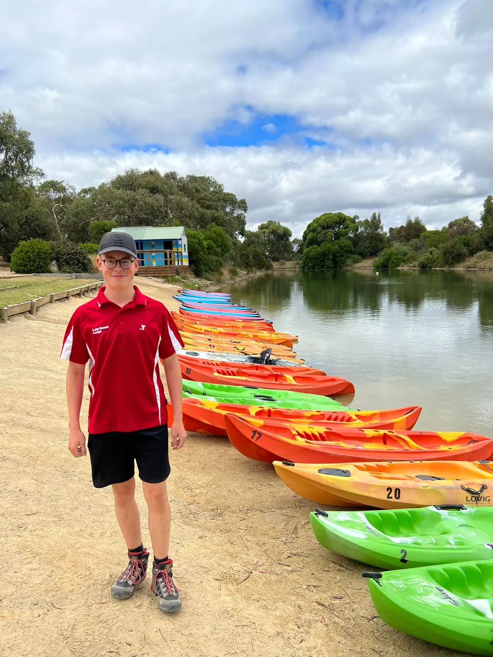 Voluntario frente a una fila de kayaks de colores junto a un lago en Australia