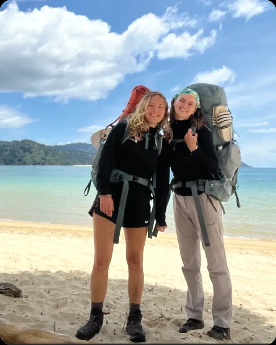Dos voluntarias con mochila en una playa de Nueva Zelanda