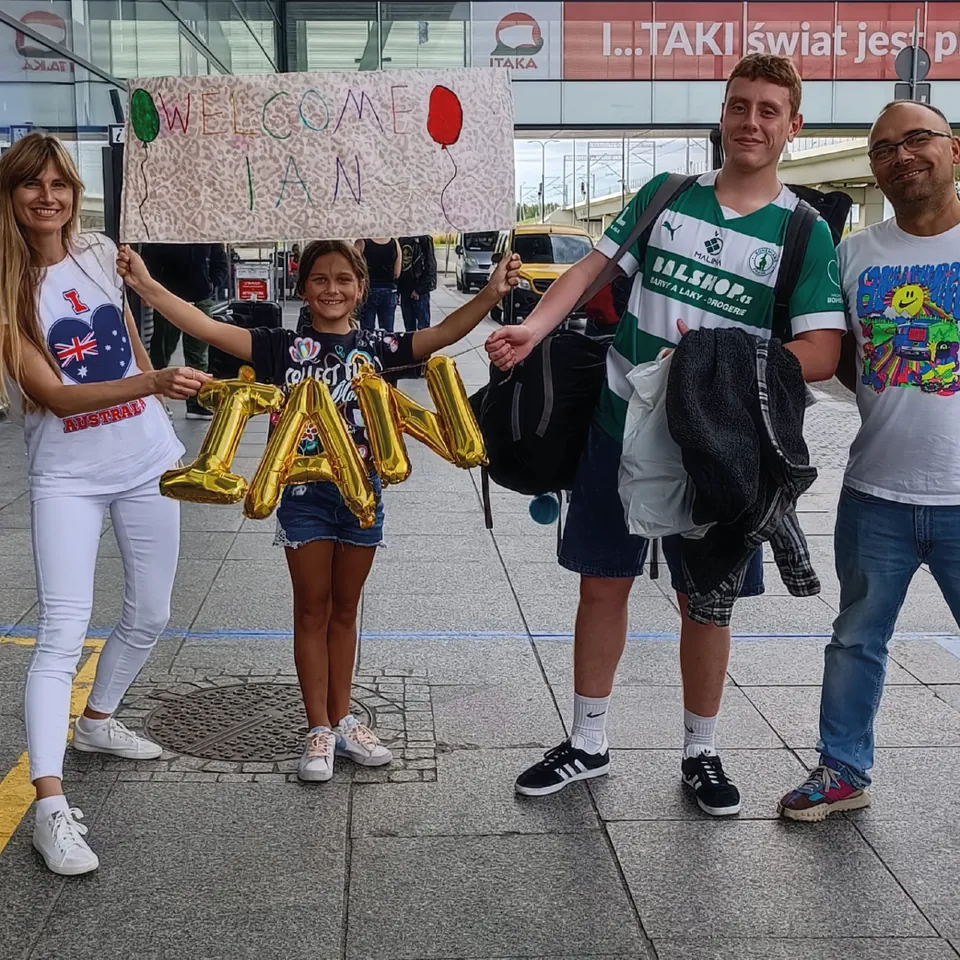 Familia anfitriona recibiendo a un voluntario en el aeropuerto con globos y un cartel